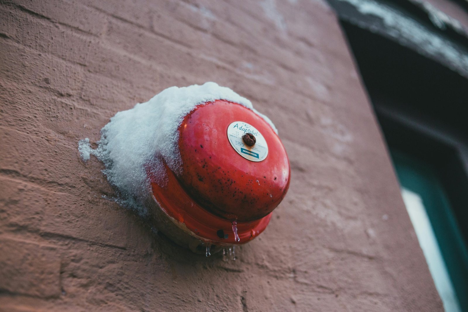 From below of fire alarm button with snow and icicles on rough wall of house in winter town